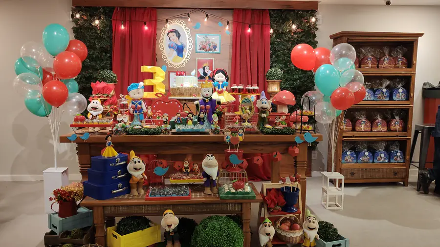 Mesa de festa com decoração de Branca de Neve: bolo, docinhos, bonecos e painel com balões