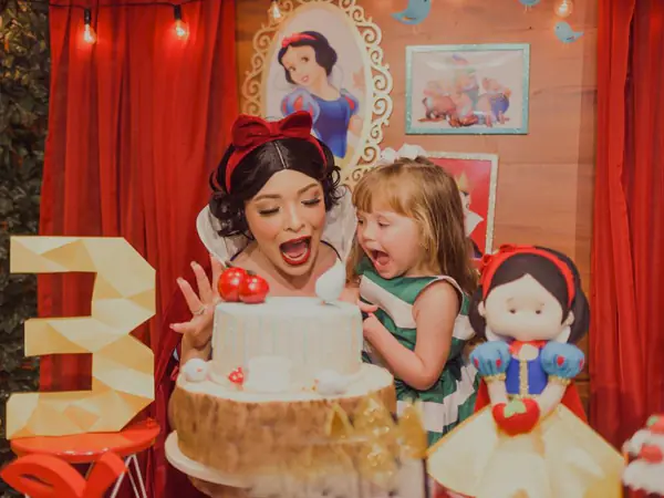 Aniversariante de 3 anos com a Branca de Neve diante do bolo, em festa na Fábrica